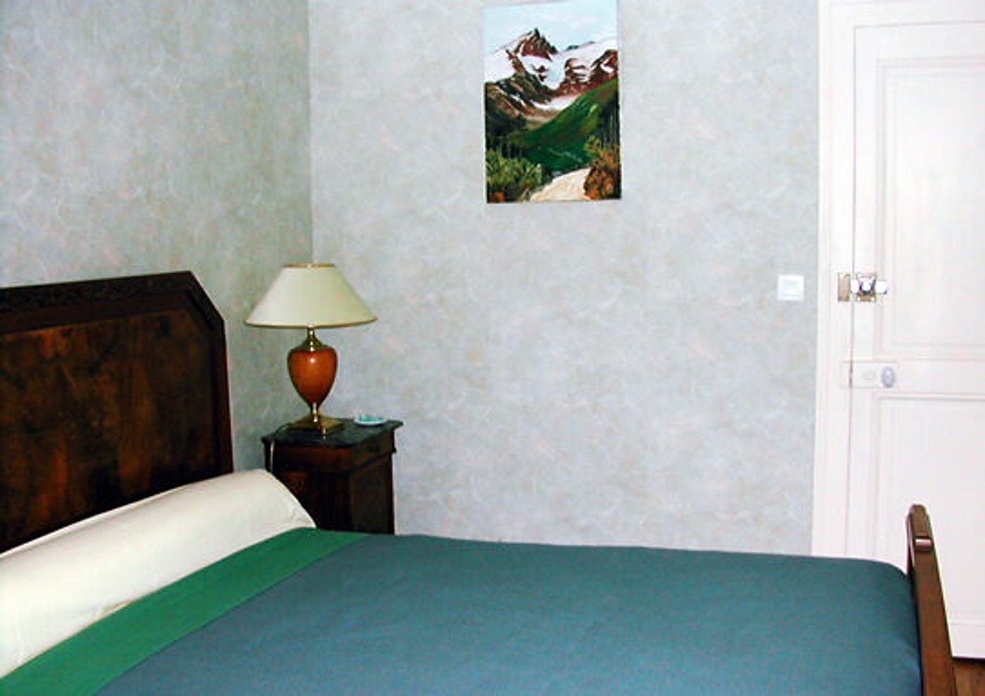 Chambre avec lit vert, table de chevet et tableau de montagne
