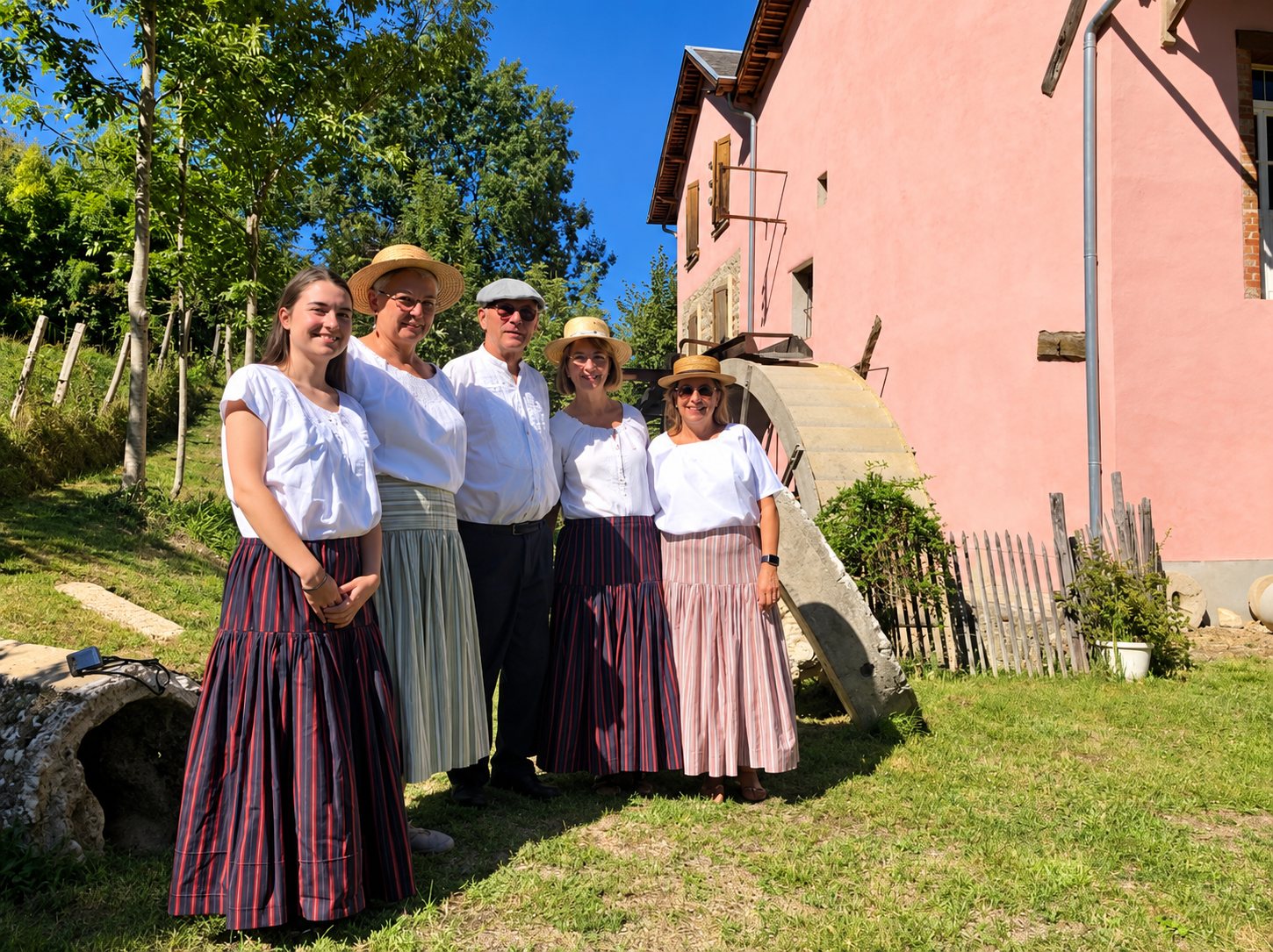 Cinq personnes en tenue traditionnelle devant le Moulin Rose et sa roue